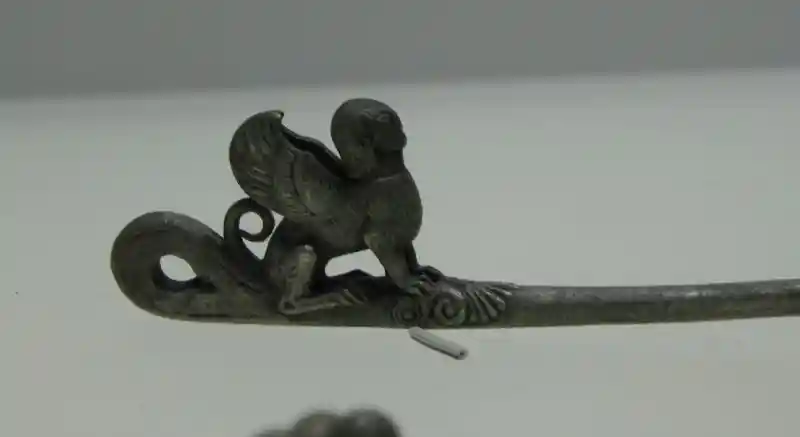 Winged man with the body of a lion on a needle-like metal.